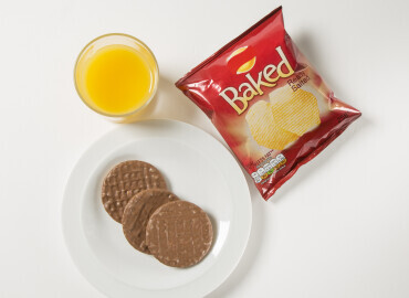 Glass of fresh orange juice with a packet of crisps and chocolate digestives